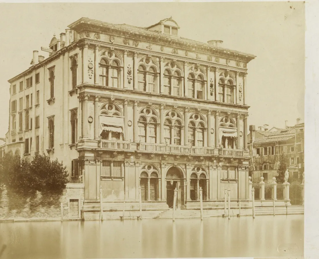 Albumen photograph of Palazzo Vendramin Calergi around 1855: the Renaissance palace seen from the Grand Canal with awnings hung over the first-floor windows, shutters closed, mooring posts in the water.