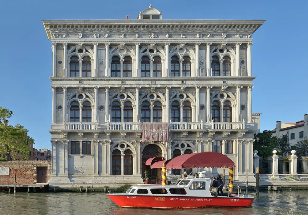 Ca' Vendramin Calergi seen across the Grand Canal: a three-storey Renaissance palace of white stone with paired round-arched windows, moored posts in the water in front of it.