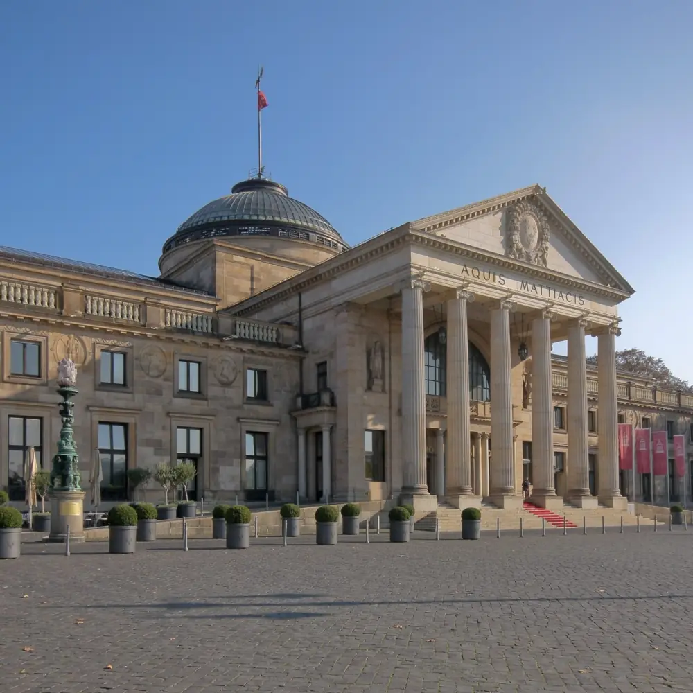 The columned portico of the Wiesbaden Kurhaus, with the inscription AQUIS MATTIACIS carved across the entablature above six tall stone columns.